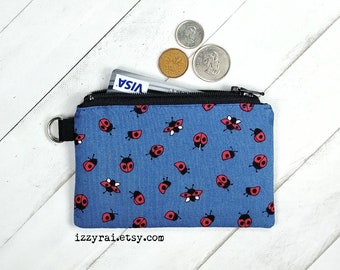 May include: A small blue zippered pouch with a ladybug print. The pouch has a black zipper and a silver ring attached to the zipper pull. The pouch is filled with a credit card and some coins.
