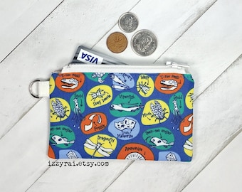 May include: A blue zippered pouch with a white zipper pull and a white strap. The pouch has a colourful print of various insects, fossils, and other natural objects. The text "izzyrai.etsy.com" is printed on the bottom of the pouch.