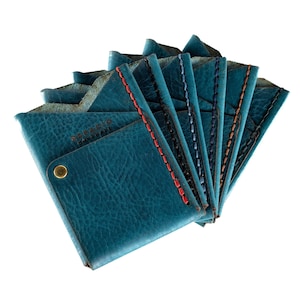 May include: A stack of teal leather wallets with contrasting colored stitching. The top wallet has the text "RESPACIO HANDMADE" embossed on the front.
