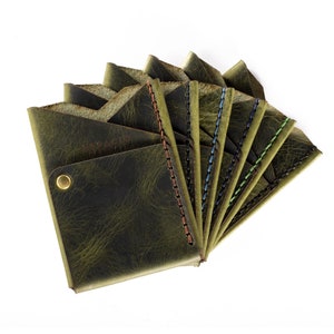 May include: A set of eight green leather wallets with different colored stitching. The wallets are arranged in a fan shape, with the stitching on the edges of each wallet visible. The wallets are made of a distressed leather, giving them a vintage look.