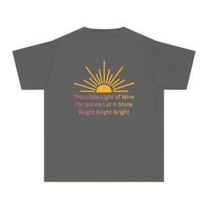 May include: Dark grey t-shirt featuring a yellow and orange sun graphic with the text "This Little Light of Mine, I'm Gonna Let It Shine, Bright Bright Bright". The shirt is made of a soft material.