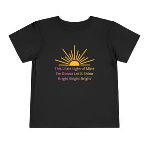 May include: Black toddler t-shirt featuring a yellow sunburst design with the text "This Little Light of Mine I'm Gonna Let It Shine Bright Bright Bright" in pink and yellow. The shirt is made of a soft material.