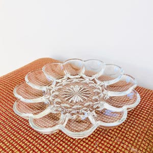 Puede incluir: Plato de servir de vidrio transparente con diseño de pétalos de flores. El centro del plato tiene un patrón de estrella. El plato está sobre una superficie estampada en rojo y dorado.