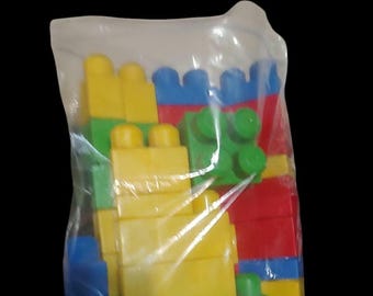 May include: A plastic bag filled with colorful building blocks. The blocks are yellow, green, blue, and red.