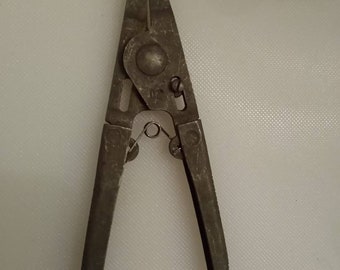May include: A pair of silver-colored pliers with a spring-loaded mechanism. The pliers have a pointed tip and a small loop on the handle.