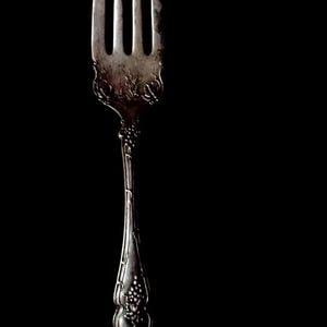 May include: A silver fork with an ornate design. The fork has three tines and a long handle with a floral pattern.