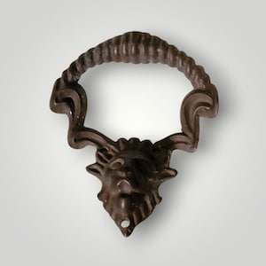 May include: A bronze-colored cabinet pull with a decorative design. The pull features a ring handle with a textured surface and a detailed face at the base. The face has a beard and horns, adding a unique touch to the hardware.