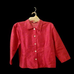 May include: A pink button-up shirt with a collar and long sleeves. The shirt has a subtle sheen and is made of a lightweight fabric.