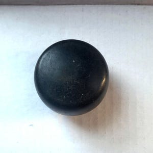May include: A dark, round knob with a slightly textured surface. The knob is a solid, matte black color and appears to be made of a durable material. The design is simple and classic, suitable for various furniture styles.