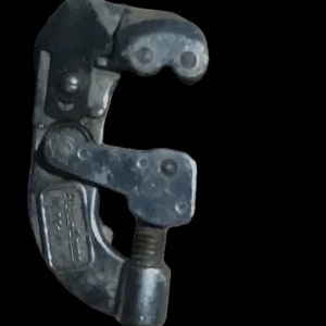 May include: A silver-colored pipe cutter tool with a red knob. The tool has a C-shaped frame with a rotating blade and a threaded adjustment screw. The tool is designed for cutting pipes.