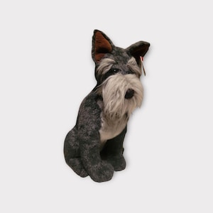 May include: A plush Schnauzer dog toy in shades of gray, black, and white, with a long, fluffy beard and upright ears. The stuffed animal is sitting, with a red tag attached.