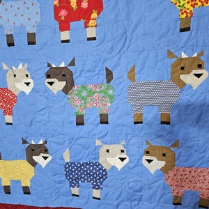 May include: A blue quilt with a patchwork design featuring various goats wearing different patterned pajamas. The goats are all facing forward and have brown legs and ears.