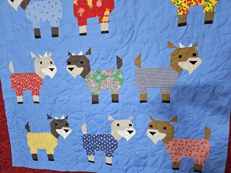 May include: A blue quilt with a patchwork design featuring various goats wearing different patterned pajamas. The goats are all facing forward and have brown legs and ears.
