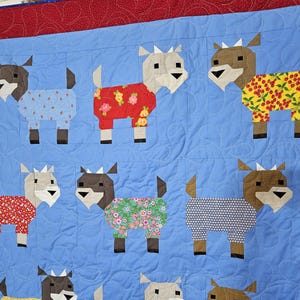 May include: A blue quilt with a red border features a pattern of nine goats wearing pajamas. The goats are made of fabric with different patterns, including floral, polka dot, and geometric designs.