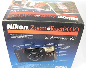 May include: A black Nikon Zoom Touch 400 camera with a 35-70mm zoom lens and accessory kit. The camera has a built-in flash and red accents. The box features the camera image and product details.
