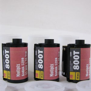 May include: Three rolls of Kodak 800T 35mm motion picture film. The film canisters are black with red and yellow labels. The labels display the film type, brand, and specifications. White plastic film canister lids are in the foreground.
