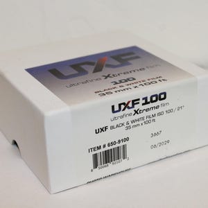 May include: A white box with black and blue text that reads "UXF 100 ultrafine Xtreme film" and "UXF BLACK & WHITE FILM ISO 100/21" with the item number "650-9100" and the date "06/2029".