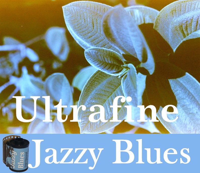 May include: A close-up of a film canister with the text "Jazzy Blues" and "Ultrafine" printed on it. The canister is on a blue background with a blurry image of green leaves in the background.