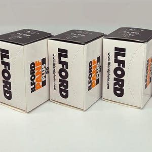 May include: Five white boxes of Ilford Pan F Plus 50 film. Each box has black text that reads "ILFORD" and "PAN F PLUS 50". The website address www.ilfordphoto.com is also printed on the boxes.