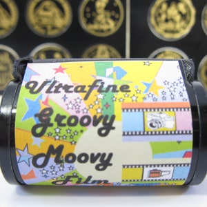 May include: A black and yellow film canister with the text "Ultrafine Groovy Moovy Film" printed on it. The canister has a colorful design with stars and film strips.