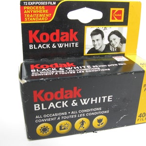 May include: A black and yellow Kodak Black & White film box. The box has the Kodak logo and text that reads "BLACK & WHITE" and "ALL OCCASIONS ALL CONDITIONS". The box also has a picture of a couple.