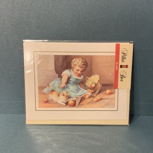 Könnte beinhalten: Eine vintage leere Grußkarte mit einem Bild eines kleinen Mädchens in einem blauen Kleid, das mit einem Kätzchen auf einem Holzboden spielt. Die Karte hat ein rotes und weißes "Pillar Box"-Logo in der oberen rechten Ecke.