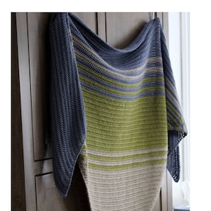 May include: A crocheted shawl in shades of blue, green, and beige. The shawl is hanging on a wooden door. The text "Winter White Knits" and "Crochet pattern" is visible at the bottom of the image.