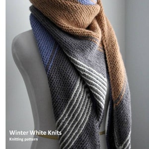 Puede incluir: Una bufanda de punto gris, azul y marrón con rayas blancas. La bufanda está drapeada sobre un maniquí blanco. El texto "Winter White Knits" y "Knitting pattern" es visible debajo de la bufanda.