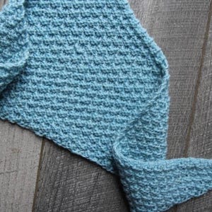 May include: A light blue triangular scarf featuring a textured, raised crochet stitch pattern. The accessory has a wide, flat central section that tapers into two elongated, pointed ends, showcasing a consistent knit-like construction throughout.