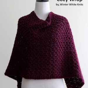 May include: A burgundy crocheted wrap made of 100% super soft wool. The wrap is displayed on a white mannequin. The text "Cozy Wrap by, Winter White Knits" is displayed above the wrap.