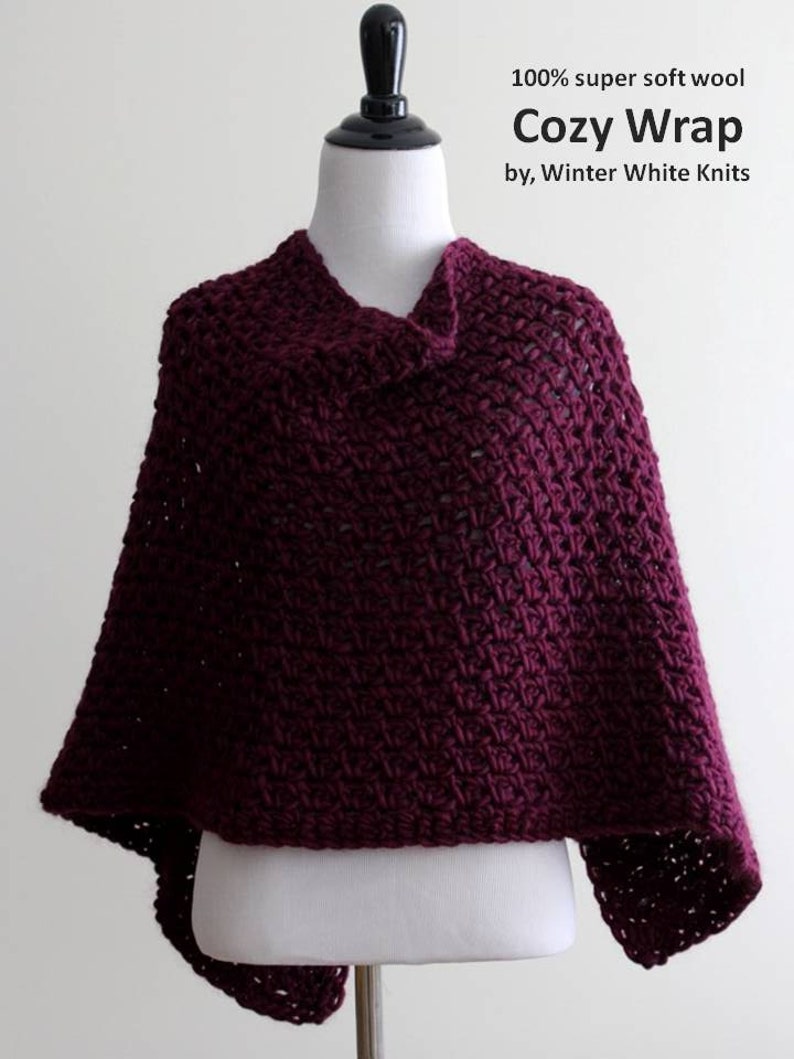 May include: A burgundy crocheted wrap made of 100% super soft wool. The wrap is displayed on a white mannequin. The text "Cozy Wrap by, Winter White Knits" is displayed above the wrap.