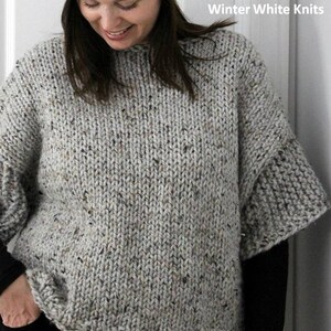 May include: A gray speckled knit sweater with a loose fit and short sleeves. The sweater is shown on a model wearing a gray knit hat. The text "KNITTING PATTERN Winter White Knits" is displayed on the right side of the image.
