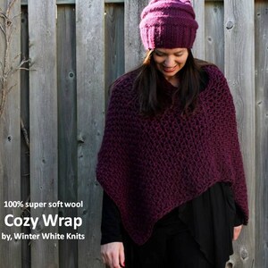 May include: A close-up of a woman wearing a deep purple knitted wrap and a matching beanie. The wrap is made of 100% super soft wool and is called "Cozy Wrap" by Winter White Knits.