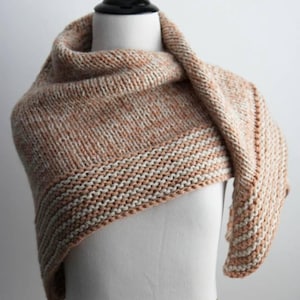 May include: A hand-knitted triangular shawl featuring a variegated peach and cream yarn in a stockinette stitch pattern. The wide border displays a textured garter stitch design alternating between peach and cream horizontal stripes.
