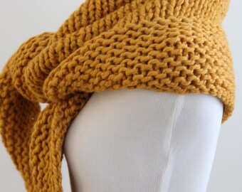 May include: A chunky knit scarf in a vibrant mustard yellow color, featuring a thick, textured garter stitch pattern. The scarf is draped around a white mannequin, showcasing its heavy, voluminous yarn construction and soft, looped appearance.
