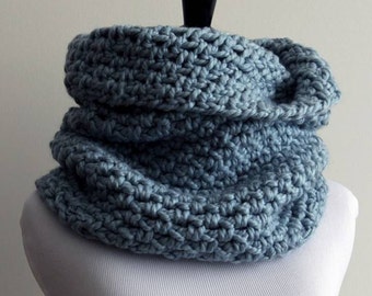May include: A cozy blue knitted cowl made with 50% wool. The cowl is displayed on a white mannequin. The text "Cozy softness, CHUNKY COWL 50% wool By, Winter White Knits" is printed below the cowl.