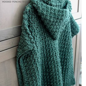 May include: A green crocheted hooded poncho vest. The vest is hanging on a wooden hanger against a woodgrain background.