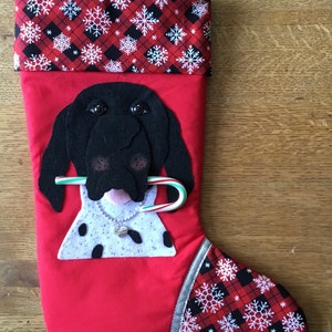 May include: Red and black Christmas stocking with a white snowflake pattern. The stocking features a black felt dog with a candy cane in its mouth.