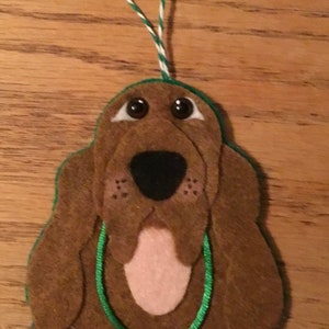 May include: A brown felt Christmas ornament shaped like a Bloodhound dog with a green ribbon and a silver heart charm that says "Merry Christmas".
