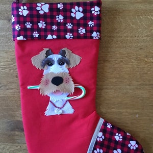 May include: Red Christmas stocking with a white dog face and a candy cane in its mouth. The stocking has a black and red plaid cuff with white paw prints.
