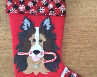 May include: Red Christmas stocking with a felt applique of a brown and white dog with a candy cane in its mouth. The stocking has a black and red plaid cuff with white snowflakes.