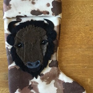 May include: A white stocking with brown spots and a felt buffalo head applique. The buffalo has black eyes and a black nose.