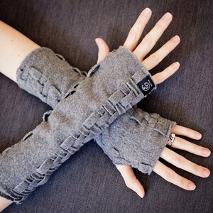 May include: Gray fingerless gloves with a braided design and a small black label that says "Knitter" on them.