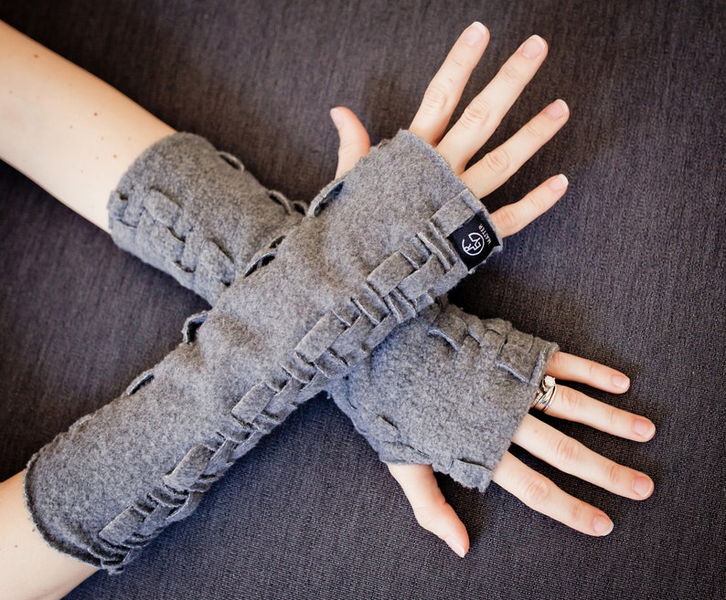 May include: Gray fingerless gloves with a braided design and a small black label that says "Knitter" on them.