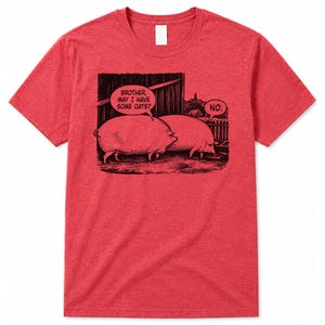 May include: A heather red short-sleeve t-shirt featuring a black ink-style graphic of two pigs in a barn. One pig asks, "Brother, may I have some oats?" and the other pig replies, "No." The design includes a wooden barn structure and a fence.