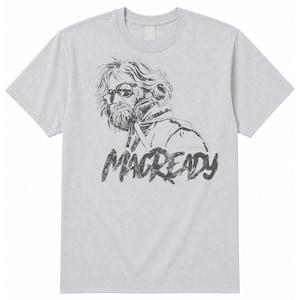 Op de afbeelding: Een lichtgrijs t-shirt met korte mouwen en een zwarte, verweerde grafische print van een persoon met baard, zonnebril en jas. Onder de illustratie staat de tekst MACREADY in een vetgedrukt, verweerd zwart lettertype.