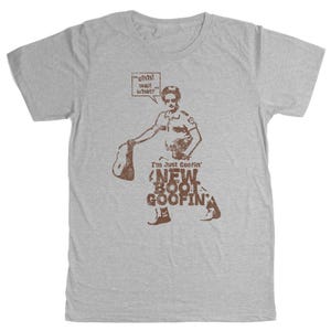 May include: A grey t-shirt with a brown graphic of a man in a police uniform holding a hat. The text on the shirt reads "I'm Just Goofin' New Boot Goofin'" and "ohh! wait what?" in a speech bubble.