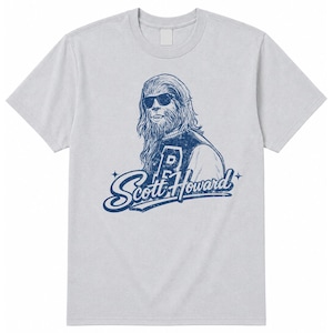 May include: A light gray short-sleeve t-shirt featuring a dark blue graphic print of a werewolf wearing sunglasses and a varsity jacket. The text "Scott Howard" is printed in a stylized script font below the character, with small star accents.
