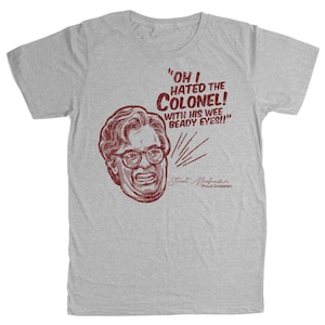Puede incluir: Camiseta gris claro con un gráfico granate desgastado de la cara de un hombre con gafas y el texto "OH I HATED THE COLONEL! WITH HIS WEE BEADY EYES!!" y "Stuart Mackenzie Proud Scotsman".