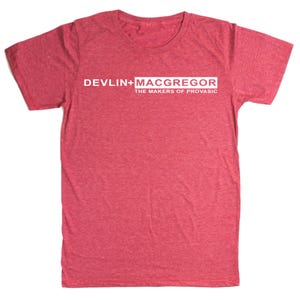 May include: A red heathered t-shirt with a crew neck. The shirt features the text "DEVLIN+MACGREGOR" in a white rectangular box, with "THE MAKERS OF PROVASIC" below it. The shirt is made of a soft, comfortable material.